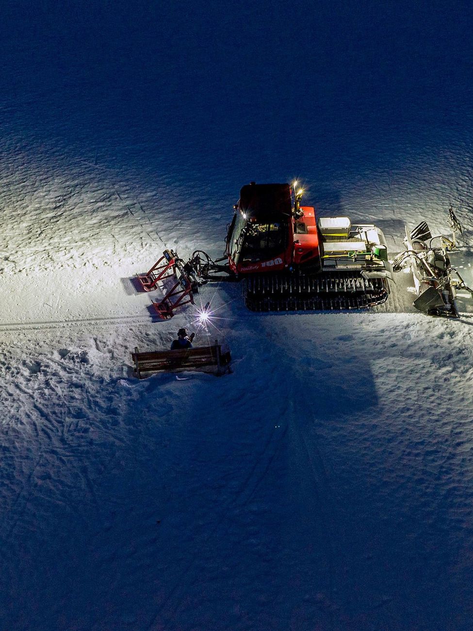 Aerial night view of a snowcat groomer working a ski slope