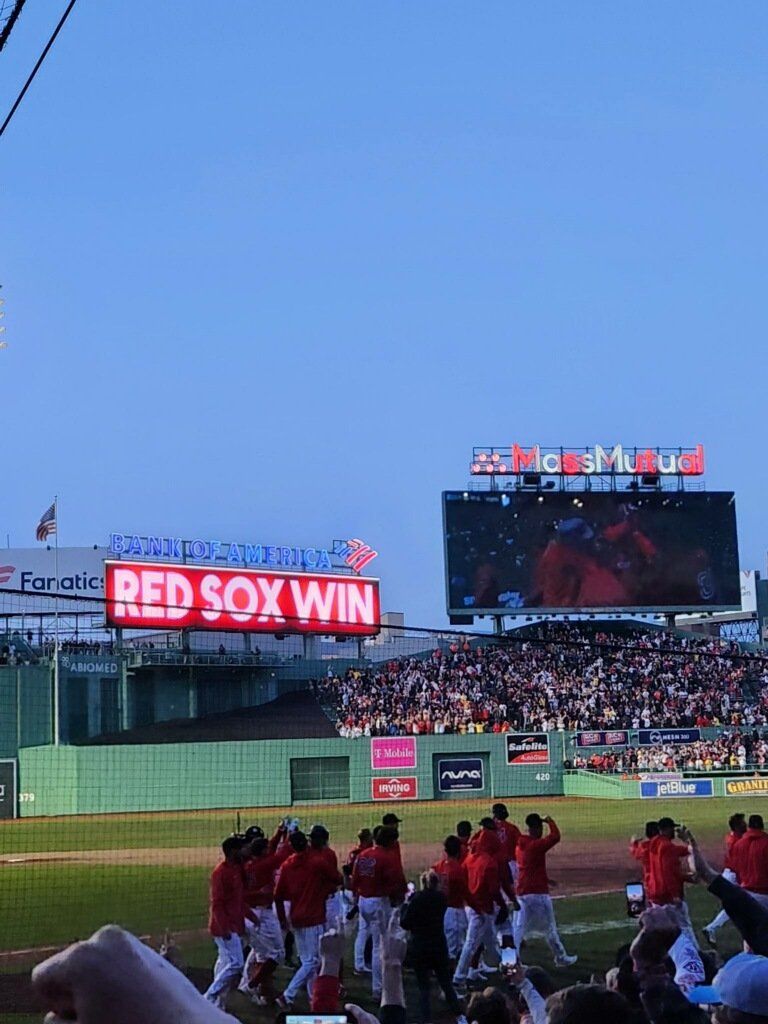 Fenway Park scoreboard reading Red Sox Win as players celebrate on the field