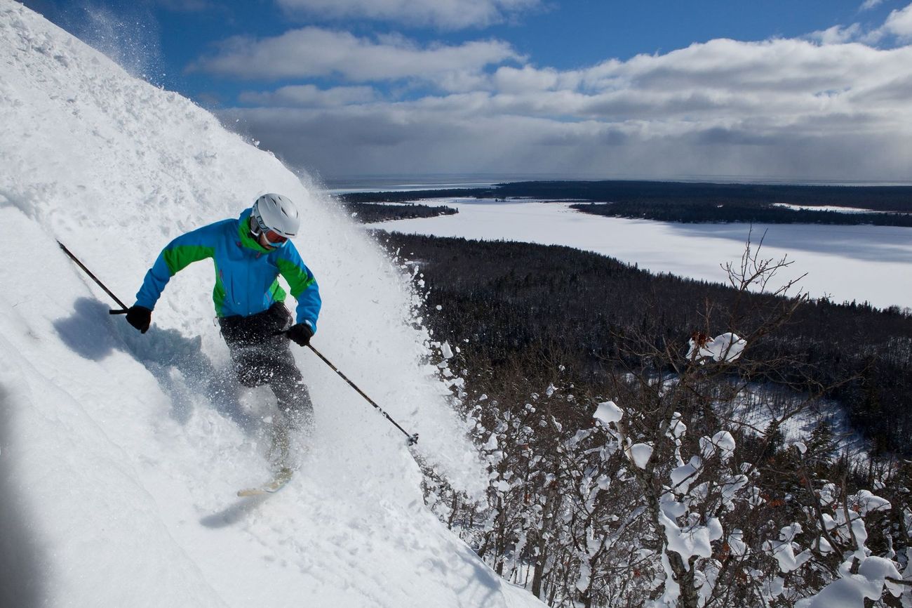 Skier carving down a steep run overlooking a frozen lake